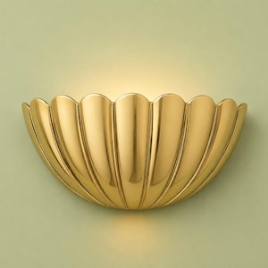 Könnte beinhalten: Eine halbkreisförmige Wandleuchte mit poliertem Gold-Finish und einem muschelartigen, gewellten Design. Die Leuchte verfügt über vertikale Rillen, die einen fächerartigen Look erzeugen und einen sanften, warmen Schein vom oberen Rand abgeben.