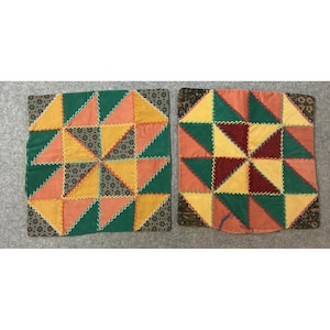 May include: Two square patchwork cushion covers featuring a pinwheel design made of triangular fabric segments in shades of green, yellow, orange, and dark red, accented with decorative yellow stitching and patterned borders on the edges.
