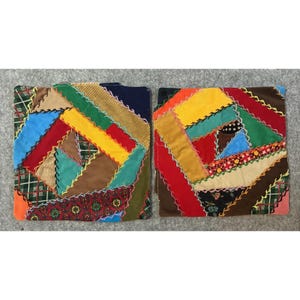 May include: Two square fabric coasters featuring a colourful crazy quilt pattern. Each coaster is constructed from various patches of corduroy, plaid, floral, and solid-coloured fabric, all joined together with visible decorative zigzag stitching.