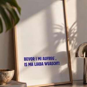 Könnte beinhalten: Ein rechteckiger Wandkunstdruck in einem hellen Holzrahmen mit weißem Hintergrund und dem blauen Text BEVOR I MI AUFREG`, IS MA LIABA WUASCHT! Der Druck ist im Hochformat gehalten und zeichnet sich durch klare Linien und ein schlichtes Design aus.