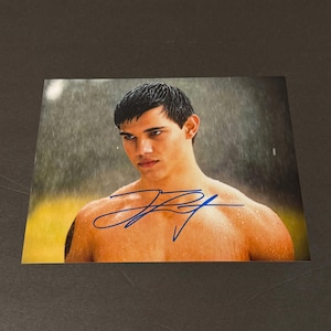 May include: A rectangular photographic print featuring a shirtless person with short dark hair, captured in a rainy outdoor setting. The image includes a prominent blue ink autograph across the chest area, signed by the individual depicted.