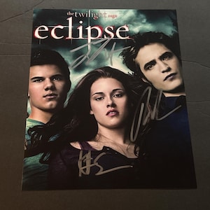 May include: A rectangular promotional print for The Twilight Saga: Eclipse featuring portraits of three actors. The title is printed in white and red text at the top. Three distinct silver ink signatures are overlaid across the image surface.