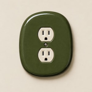 May include: A glossy olive green oval wall plate cover featuring a standard dual electrical outlet with two white receptacles. The plate has a smooth, rounded edge design and is secured by a single central metal screw between the two sockets.