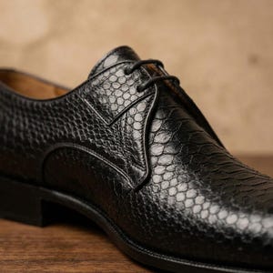 Handmade black derby shoes featuring an exotic python-pattern texture, classic lace-up design, polished finish, premium leather construction, and elegant formal silhouette for men.
