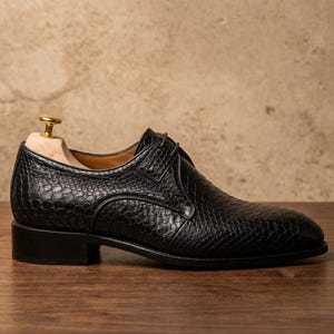 Handmade black derby shoes featuring an exotic python-pattern texture, classic lace-up design, polished finish, premium leather construction, and elegant formal silhouette for men.