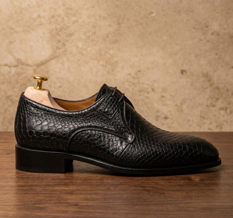 Handmade black derby shoes featuring an exotic python-pattern texture, classic lace-up design, polished finish, premium leather construction, and elegant formal silhouette for men.