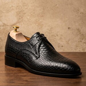 Handmade black derby shoes featuring an exotic python-pattern texture, classic lace-up design, polished finish, premium leather construction, and elegant formal silhouette for men.