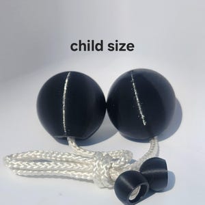 May include: Two black spherical balls connected by a white braided rope, featuring a visible seam line on each sphere. The text 'child size' is printed above the spheres. Two smaller black cylindrical components are attached to the rope ends.