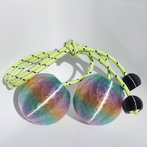 May include: A pair of spherical, iridescent rainbow-colored balls with a textured scale pattern, attached to a neon yellow rope with black flecks. The rope features a central knot and two black spherical beads at the ends of the cord.
