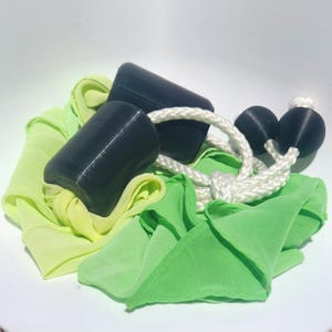 May include: A set of two black cylindrical weights attached to a thick white braided rope, paired with flowing lime green and yellow fabric. The weights are smooth and solid, while the rope features a knotted design connecting the components.