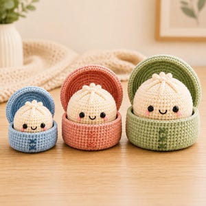 Puede incluir: Tres juguetes de albóndigas de ganchillo de diferentes tamaños, cada uno con una cara de color crema con ojos negros y una boca sonriente. Las albóndigas están dentro de recipientes de ganchillo a juego en azul, rosa y verde.