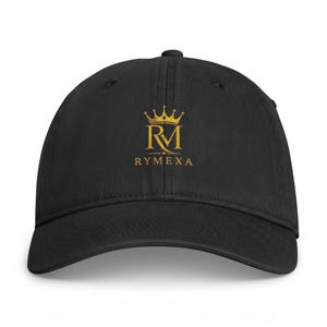 Pode incluir: Um boné de beisebol preto com um logótipo dourado bordado na parte da frente. O logótipo consiste numa coroa estilizada posicionada acima das letras RM, com o texto RYMEXA impresso em letras maiúsculas douradas por baixo do monograma.