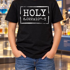 以下が含まれることがあります： 中央に「HOLY 6.022x10^23-Y」というテキストがプリントされた、白い長方形のグラフィックが特徴の黒い半袖Tシャツ。デザインには、無地の黒い生地と対照的な、かすれた質感の白いフォントと枠線が使用されています。