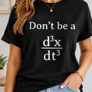 May include: A black short-sleeved t-shirt featuring the white printed text 'Don't be a' above a mathematical derivative symbol representing the third derivative of position with respect to time, which is commonly known as a jerk.