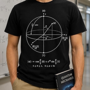 Può includere: Una t-shirt nera a maniche corte con una stampa grafica bianca di un diagramma della sfera di Bloch utilizzato nella meccanica quantistica. Il design include notazioni matematiche, assi etichettati x, y, z e l'equazione |ψ⟩ = cos(θ/2)|0⟩ + e^iφ sin(θ/2)|1⟩.