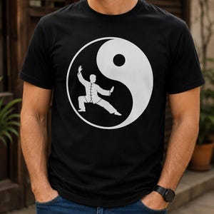 Könnte beinhalten: Ein schwarzes kurzärmeliges T-Shirt mit einer großen weißen Grafik auf der Brust. Die Grafik zeigt ein Yin-und-Yang-Symbol mit der Silhouette einer Person, die eine Kampfkunstpose innerhalb des weißen Bereichs des kreisförmigen Designs einnimmt.