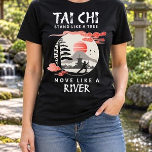 以下が含まれることがあります： TAI CHI STAND LIKE A TREE MOVE LIKE A RIVERという文字がプリントされた黒の半袖Tシャツ。デザインには、赤い太陽、太極拳をする人のシルエット、塔、木、赤い雲が描かれています。