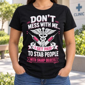 May include: A black short-sleeved t-shirt featuring a white and pink graphic design. The text reads DON'T MESS WITH ME... I GET PAID TO STAB PEOPLE WITH SHARP OBJECTS. The design includes a caduceus symbol flanked by two syringes with pink liquid.