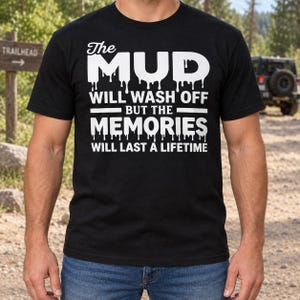 Op de afbeelding: Een zwart t-shirt met korte mouwen en witte tekst: The MUD WILL WASH OFF BUT THE MEMORIES WILL LAST A LIFETIME. De woorden MUD en MEMORIES zijn ontworpen met een druipend effect aan de onderkant van de letters.