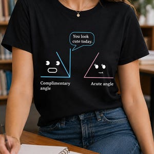 May include: A black short-sleeve t-shirt featuring a graphic of two geometric shapes with faces. One blue shape is labelled Complimentary angle, and one pink shape is labelled Acute angle. A speech bubble says, You look cute today.