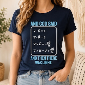 May include: A navy blue short-sleeved t-shirt featuring the text AND GOD SAID in light blue, followed by a white rectangular graphic displaying Maxwell's equations, and the text AND THEN THERE WAS LIGHT in light blue at the bottom of the design.