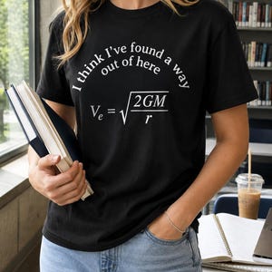 Op de afbeelding: Een zwart T-shirt met korte mouwen en witte tekst "I think I've found a way out of here" boven de natuurkundige formule voor ontsnappingssnelheid "Ve = vierkantswortel van 2GM gedeeld door r" gedrukt in een helder wit lettertype.
