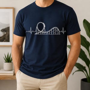 以下が含まれることがあります： 胸元に白いグラフィックプリントが施されたネイビーブルーの半袖Tシャツ。デザインは、連続する心拍数のラインが、ループと小さな丘を持つジェットコースターのシルエットへと変化していく様子を描いています。