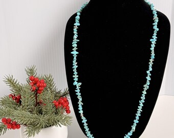 Può includere: Una collana lunga composta da piccole pietre irregolari di colore azzurro turchese infilate insieme. La collana è esposta su un busto nero, creando un contrasto con le tonalità blu brillante delle perle di pietra.