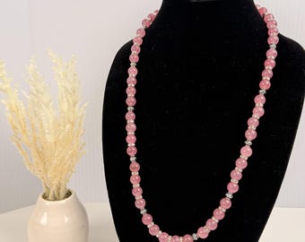 Può includere: Una collana lunga caratterizzata da perline rotonde e traslucide di colore rosa, alternate a distanziatori cilindrici più piccoli color argento. Le perline sono di dimensioni uniformi e disposte in un unico filo continuo.