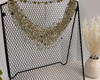 Può includere: Una collana importante a più fili caratterizzata da una densa disposizione di piccole perline sfaccettate nei toni del verde oliva, ambra, oro e vetro trasparente. La collana è realizzata con un design a rete metallica e una catenina.