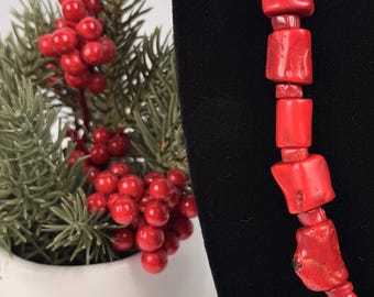 Può includere: Una collana composta da perline irregolari di colore rosso vivace, levigate e simili a pietre, infilate insieme. Le perline variano per forma e dimensione, creando un aspetto strutturato lungo il filo. La collana è esposta su uno sfondo nero.