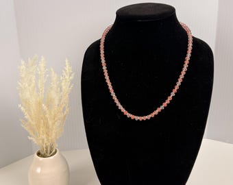 Può includere: Una collana di perline con un motivo ripetitivo di piccole perline rotonde rosa traslucide e perline di cristallo trasparente sfaccettato. La collana è esposta su un busto in velluto nero, che mette in risalto la disposizione uniforme.