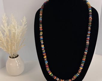 Può includere: Una collana lunga composta da un unico filo di piccole perline piatte e circolari in una varietà di colori vivaci, tra cui rosso, blu, giallo, verde e arancione. Le perline sono disposte in un cerchio continuo, creando un motivo multicolore.