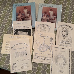 May include: A collection of eight vintage smocking patterns for crafting projects. The patterns feature designs for a neckroll pillow, a baby bonnet, a Christmas wreath, a bird, and a puffy pleats pillow. The patterns are printed on white paper with black ink and include instructions and diagrams.