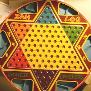 May include: A round Chinese Checkers board with a star-shaped design. The board features a yellow center with brown pegs and colored triangles in red, orange, green, and blue. The words "SAN" and "LOO" are at the top, and "CHINESE CHECKERS" is at the bottom.
