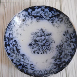 May include: Antique blue and white floral plate. The plate features a central floral bouquet and a border of stylized flowers and leaves. The plate has a slightly worn appearance, adding to its vintage charm.
