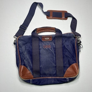 May include: A navy blue canvas briefcase with brown leather corner accents and handles. It features a Lands' End label, a detachable shoulder strap with a brown pad, and the embroidered initials SRB in red on the front center of the bag.