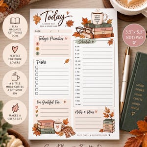 Pode incluir: Um bloco de notas de planejamento diário de 14 cm por 21,6 cm com tema de outono, folhas secas, pilhas de livros e xícaras de café. O layout inclui seções para prioridades, tarefas, um cronograma das 6h às 22h, gratidão e notas.