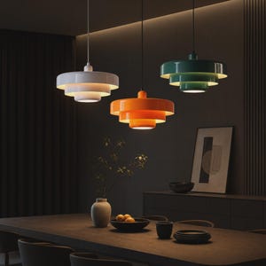 May include: Three tiered pendant lights hanging from the ceiling, featuring a white, an orange, and a dark green glossy finish. Each lamp has a circular, multi-layered design that directs light downward, creating a focused illumination effect.