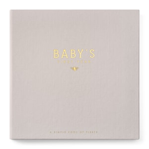May include: A gray linen-covered book with gold foil lettering that reads "BABY'S FIRST YEAR" and "A SIMPLE BOOK OF FIRSTS". A small gold bee icon is centered below the title.