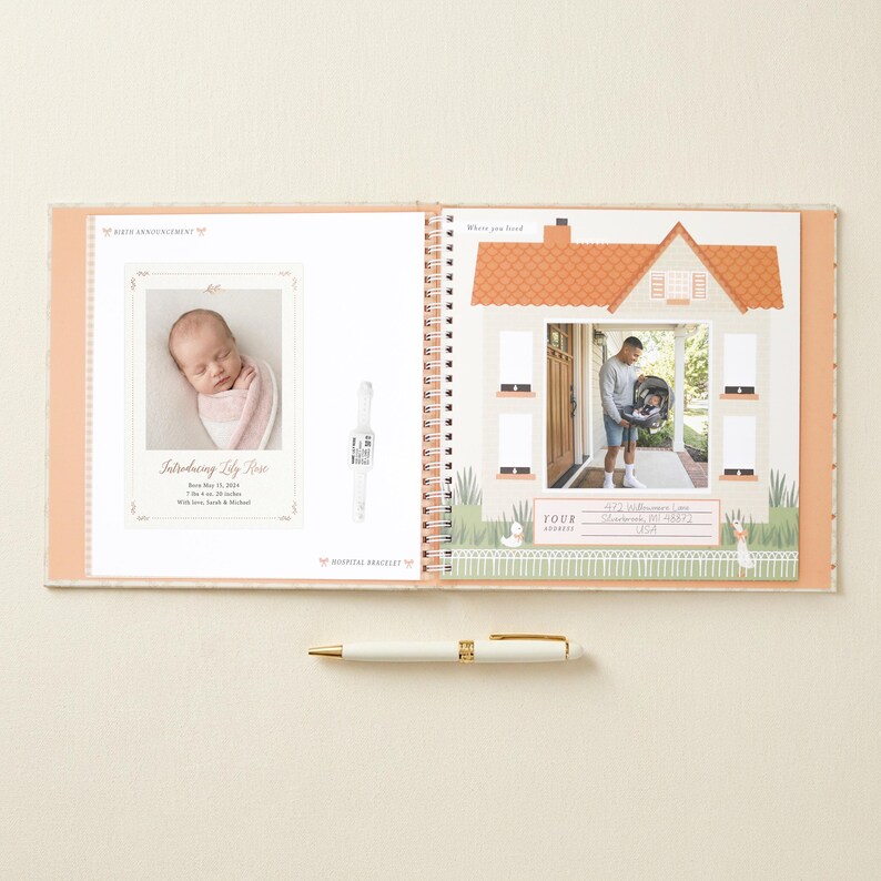 May include: A spiral-bound baby memory book open to two pages. The left page features a birth announcement for Lily Rose with a photo of a newborn, text details, and a hospital bracelet. The right page shows a house illustration with a photo of a person holding a baby carrier and an address section. A white and gold pen lies horizontally below the book.