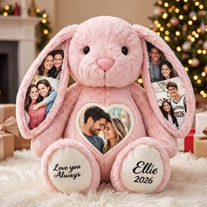 May include: A plush pink rabbit stuffed animal featuring custom photo prints on its long ears and a heart-shaped photo frame on its chest. The white foot pads are embroidered with the black text Love you Always and Ellie 2026.
