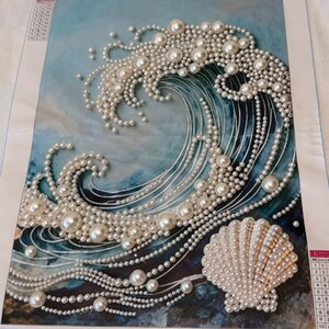 May include: A diamond painting kit featuring a blue ocean wave design embellished with white faux pearls of varying sizes. A large seashell is positioned in the lower right corner, also covered in pearls. The canvas measures 30x40cm.