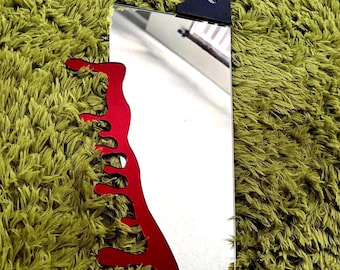 May include: A decorative prop shaped like a large kitchen cleaver with a reflective silver blade and a black handle. The blade features a prominent red cutout design along one edge that mimics the appearance of dripping liquid.
