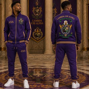 Könnte beinhalten: Ein violetter Trainingsanzug mit goldenen Streifen an Ärmeln und Beinen. Die Jacke hat einen goldenen Reißverschluss, die Buchstaben AXA auf der Brust und ein Lambda Chi Alpha Wappen. Der Rücken zeigt das gestickte Lambda Chi Alpha Wappen.