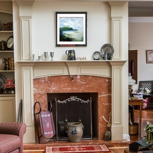 May include: A fireplace with a white mantel and a marble surround. The fireplace has a black metal grate and a red brick hearth. There is a painting above the mantel and a vase on the mantel.