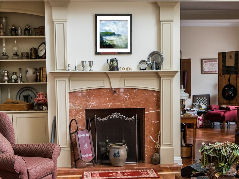 May include: A fireplace with a white mantel and a marble surround. The fireplace has a black metal grate and a red brick hearth. There is a painting above the mantel and a vase on the mantel.