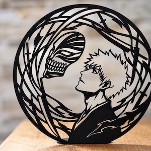 Könnte beinhalten: Ein kreisförmiges Kunstwerk aus schwarzem Metall mit einem Scherenschnitt-Design, das das Profil einer Figur mit stacheligen Haaren zeigt, die einer totenkopfartigen Maske gegenübersteht, umgeben von geschwungenen Linien und Schwertformen.