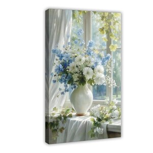 May include: A white ceramic vase filled with a bouquet of blue and white flowers sits on a draped white cloth. The arrangement is positioned in front of a window with sheer white curtains and green foliage visible through the glass panes.