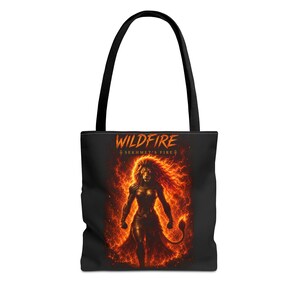 Könnte beinhalten: Eine schwarze Tragetasche mit einem Grafikdruck einer löwenköpfigen Figur, die von orangefarbenen und roten Flammen umgeben ist. Der Text "WILDFIRE" steht oben in Orange, gefolgt von dem kleineren Text "SEKHMET'S FIRE" mit einem Ankh-Symbol auf jeder Seite.